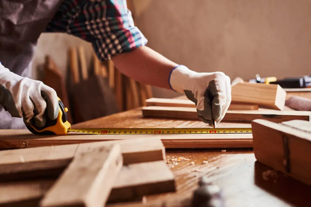 craftsmen use tape measure to assemble wooden pieces Construction Worker hold ruler Professional carpenter at work measuring wooden planks for custom cabinetry in Boca Raton